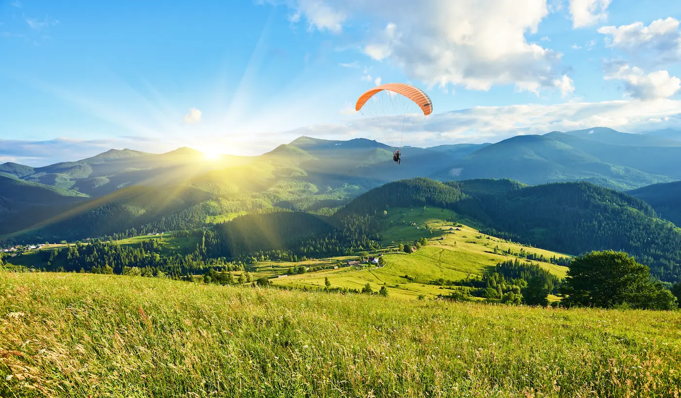 Piloto de parapente sobre colinas verdes y montañas en verano